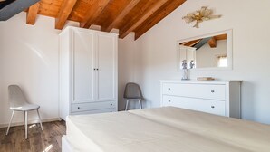 Une chambre avec un plafond en bois, une armoire blanche, un lit, une chaise et une commode.