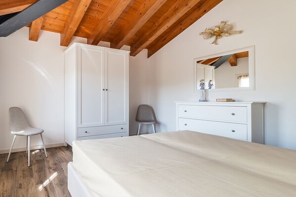 A bedroom with a wooden ceiling, white wardrobe, a bed, a chair, and a dresser.