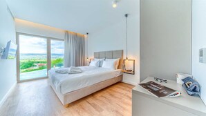 Una habitación de hotel moderna con una cama grande, una mesita de noche con lámpara, vistas al campo y un pequeño escritorio con silla.