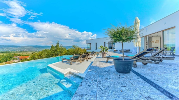 Una piscina infinita con sillones de descanso, un árbol en maceta y vistas del paisaje.