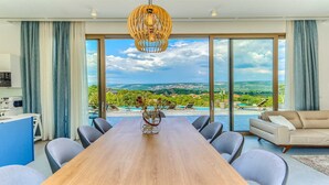 Un comedor amplio con una mesa de madera, sillas modernas y vistas a una piscina y jardines a través de grandes ventanales.