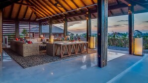 Un amplio salón al aire libre con techos altos, una mesa de madera con cojines de colores y vistas al paisaje circundante.