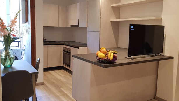 Eine kompakte Küche mit integriertem Backofen, eine kleine Essecke mit Tisch und Stühlen sowie ein an der Wand befestigter Fernseher.