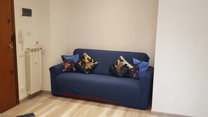 Ein blaues Sofa mit dekorativen Kissen in einem Raum mit Holzboden und einem weißen Heizkörper.
