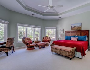 A bedroom with a large bed, two wicker chairs, a ceiling fan, and large windows. - Something for everyone- private pool on the water and pool table! (Hilton Head)