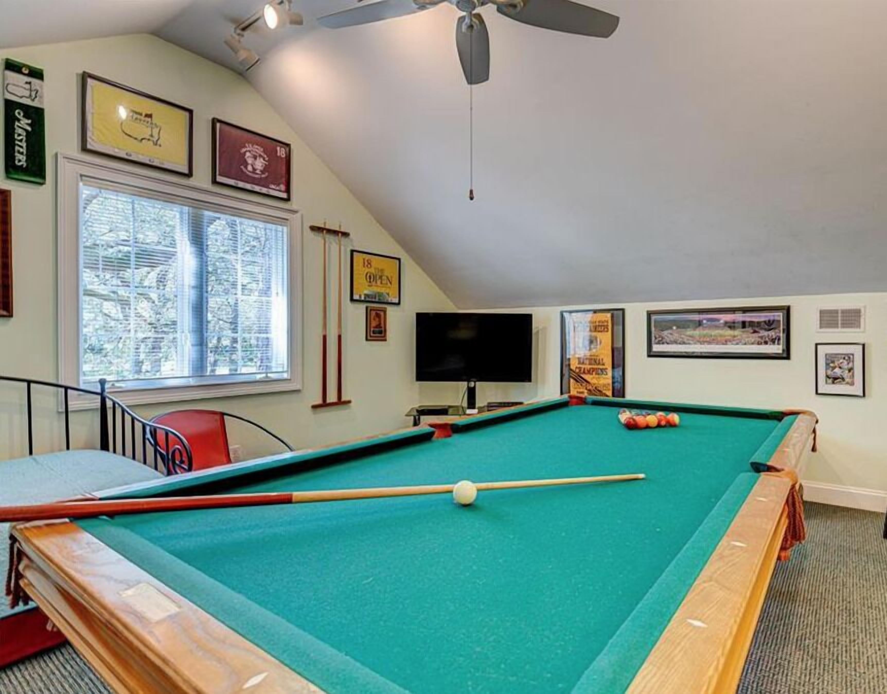 A pool table in a room with a ceiling fan, a TV, and framed pictures on the walls.
