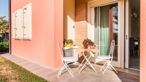 A patio with two white chairs and a table, a sliding glass door, and a small garden area with plants.