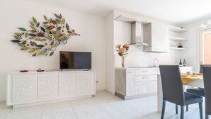 A modern kitchen with white cabinetry, a flat-screen TV on a white console, and a dining area with two chairs.