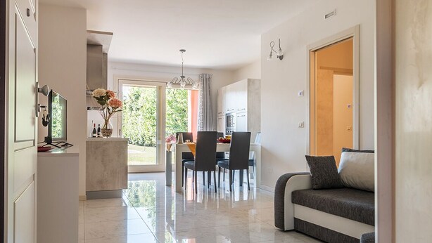 A modern kitchen with white cabinets, a dining area with a table and chairs, and a living area with a sofa.
