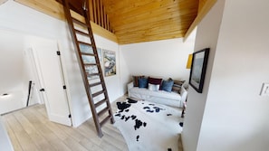 Un dormitorio con una escalera de madera, una cama con funda de piel de vaca y un cartel en la pared.