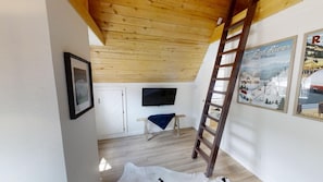 Una habitación con techo de madera, televisor montado en la pared, una escalera y un cartel de un complejo de esquí.