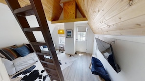Quarto estilo loft com teto de madeira, escada, sofá, televisão e tapete de couro.