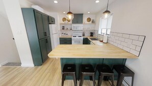 A modern kitchen with a central island, dark green cabinets, white appliances, and pendant lighting. - Das Hartmann Haus - In Town - WiFi - Washer/Dryer - Grill - Fireplace (Red River)
