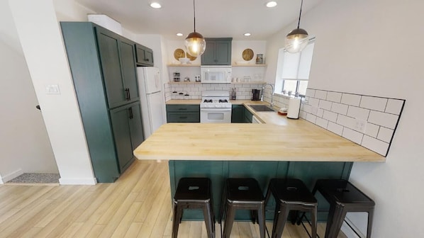 Una cocina moderna con una isla central, armarios verde oscuro, electrodomésticos blancos e iluminación colgante.
