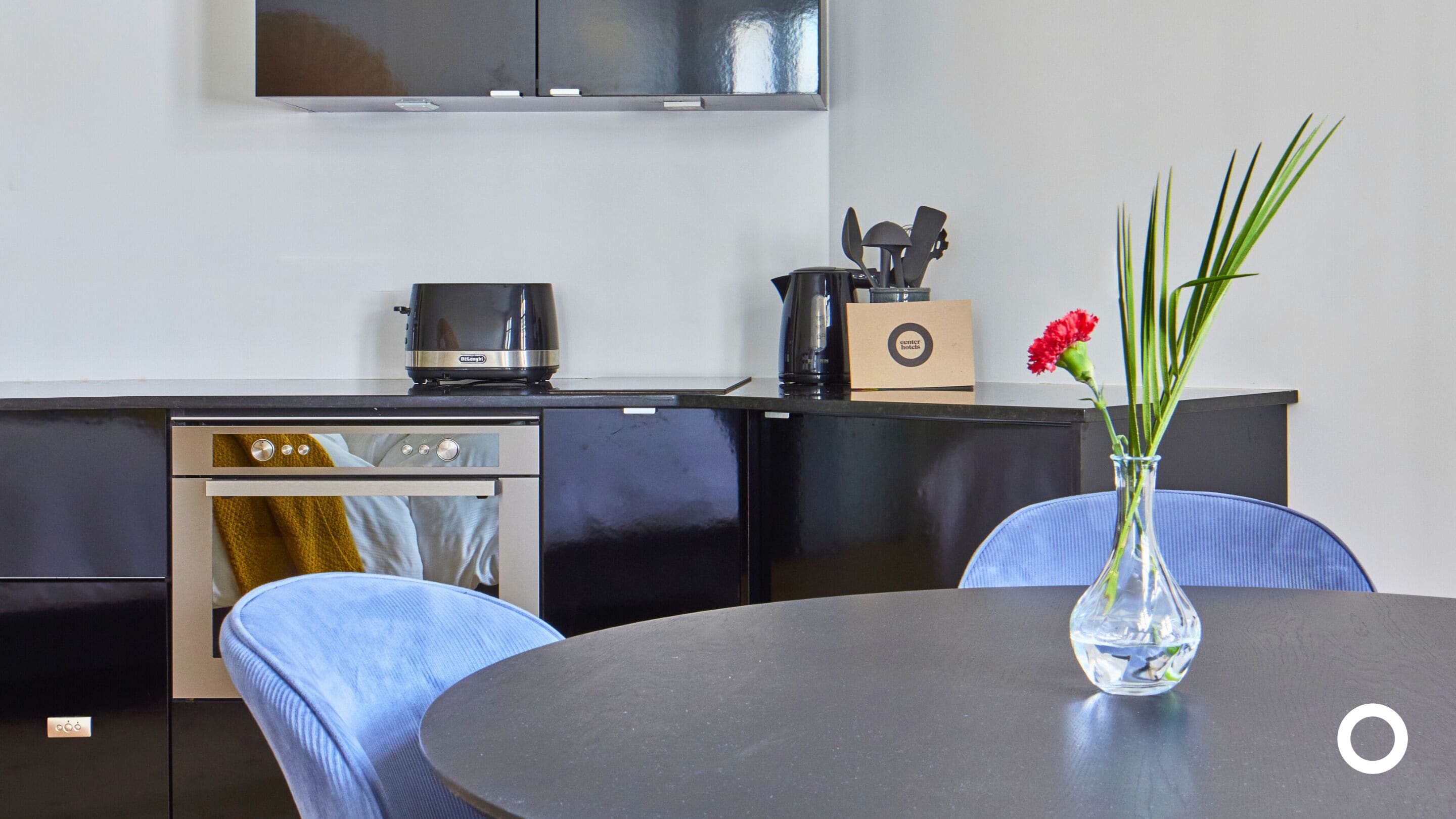 A modern kitchen with a stove, oven, and coffee maker. There is a vase with flowers on a table.