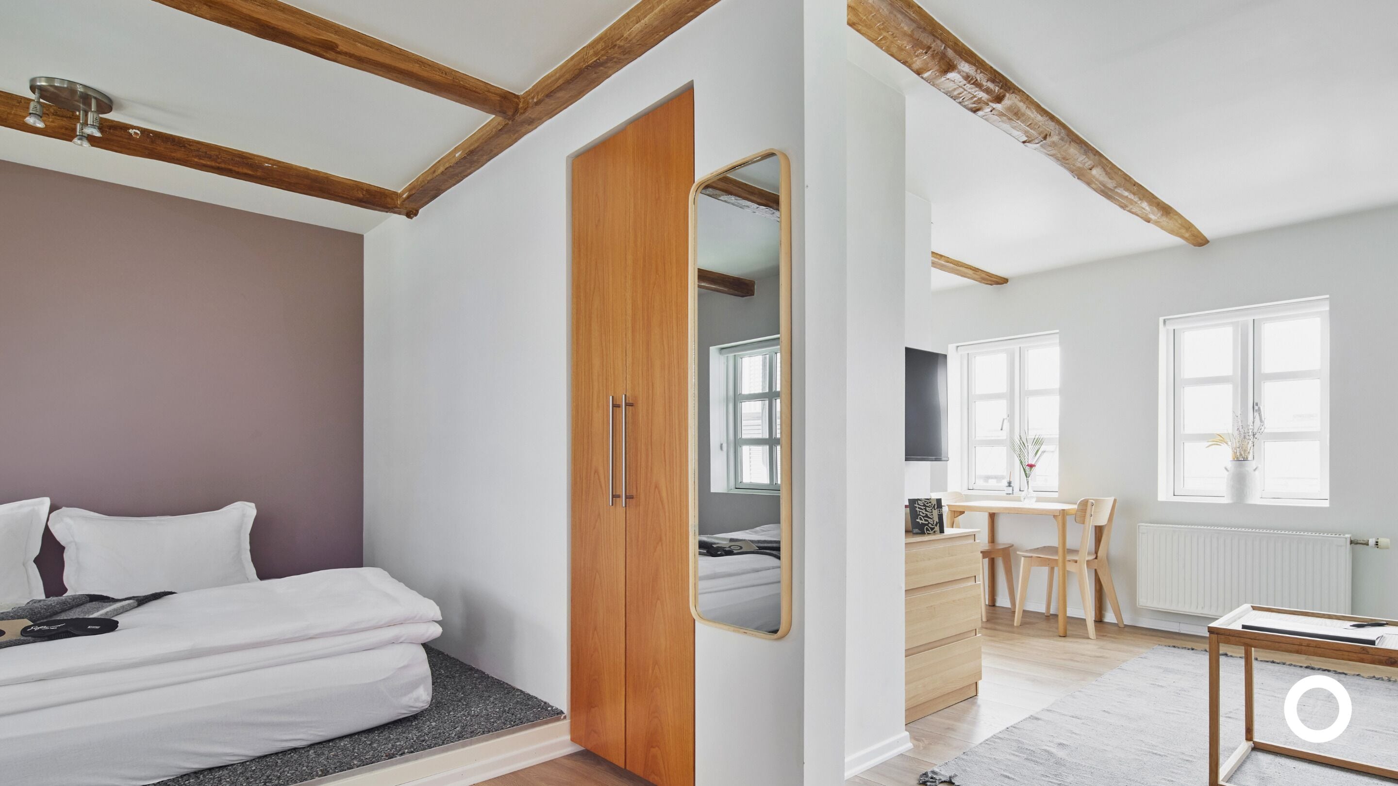 Un dormitorio con cama, armario de madera y una pequeña cocina con mesa y sillas.
