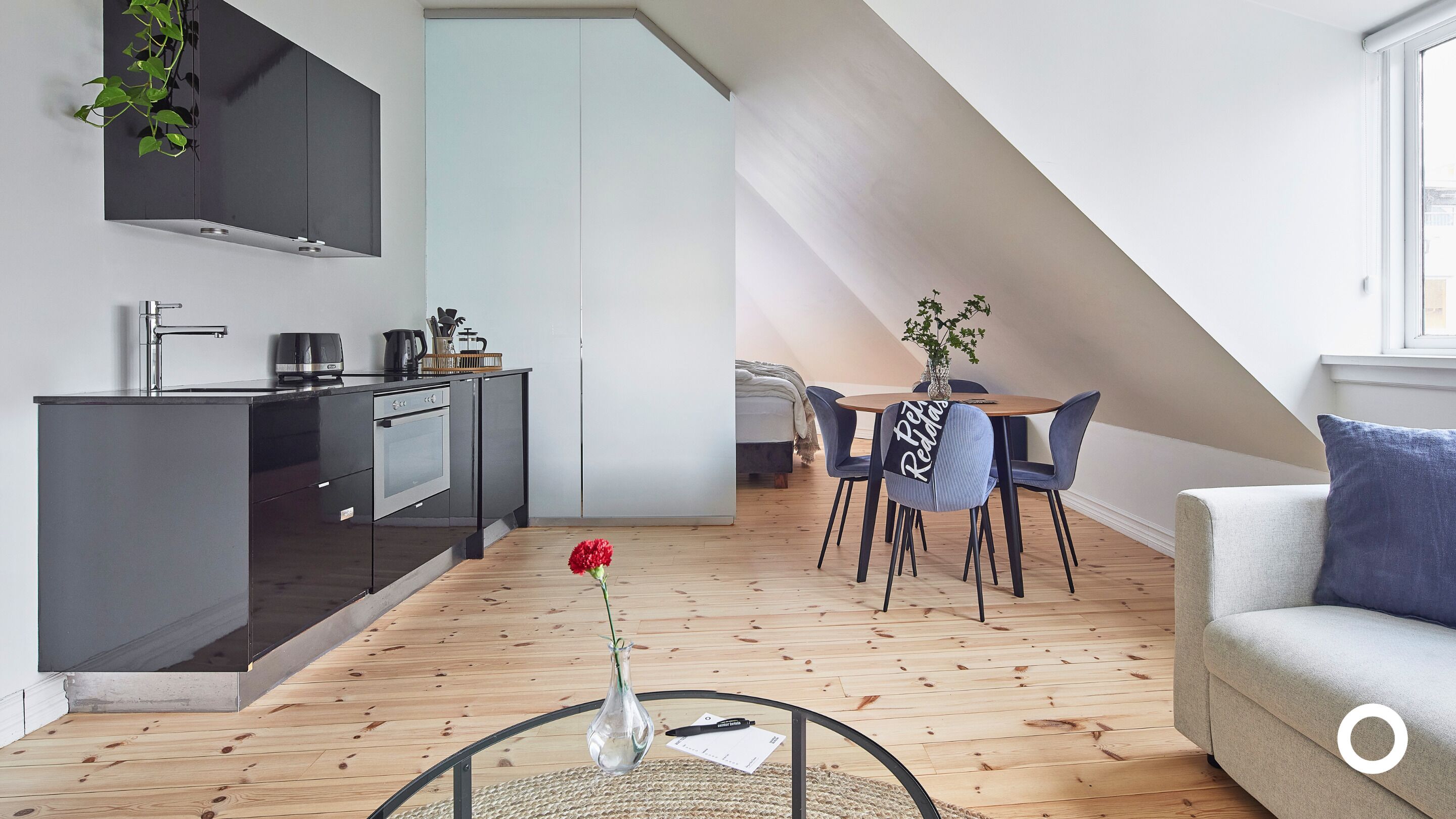 A modern kitchen with dark cabinetry, a dining area with a round table and chairs, and a living area with a sofa and a coffee table.