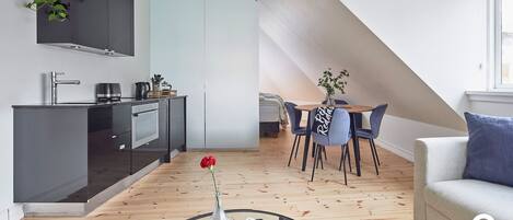 Et moderne køkken med mørke skabe, et spiseområde med et rundt bord og stole, samt en opholdsstue med sofa og sofabord.