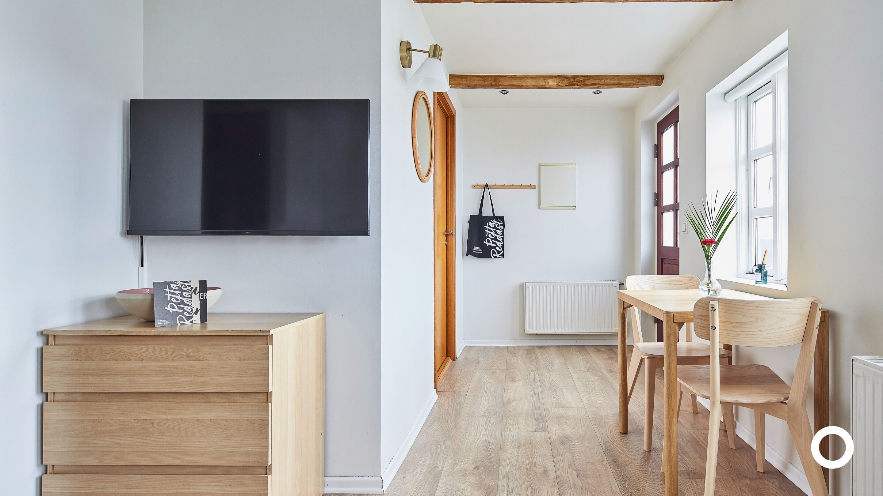 Una sala moderna con televisor de pantalla plana, muebles de madera, una mesa de comedor con sillas, una ventana con vistas y un radiador.