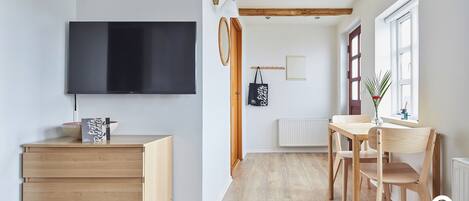 Una sala moderna con televisor de pantalla plana, muebles de madera, una mesa de comedor con sillas, una ventana con vistas y un radiador.