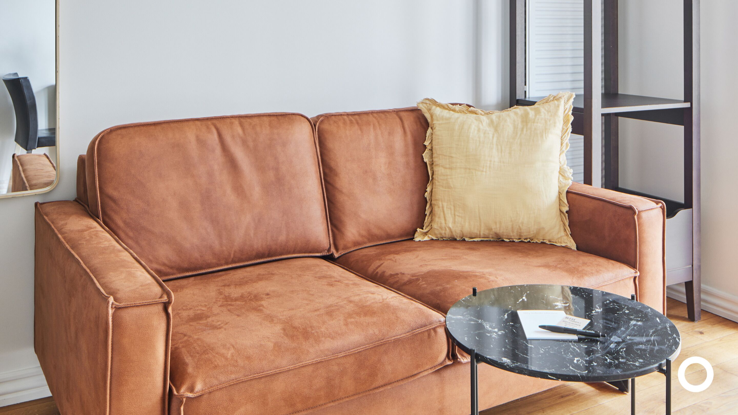 A brown leather sofa with a ruffled pillow, a black marble coffee table, and a mirror on the wall.