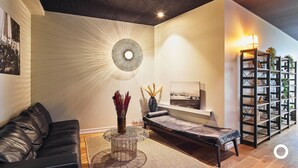 A modern living room with a black leather sofa, a bench, a decorative wall piece, and a bookshelf.