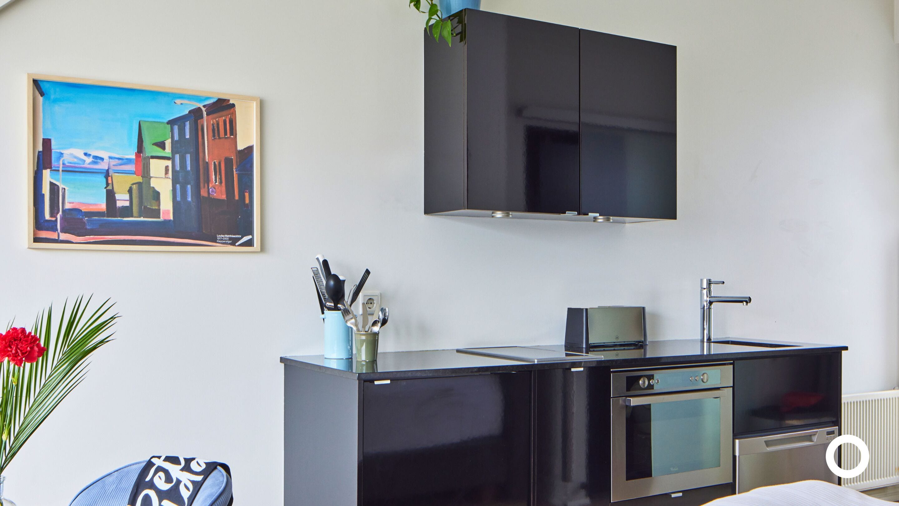 A modern kitchen with a black countertop, a built-in oven, and a microwave. There is a framed painting on the wall above the counter.