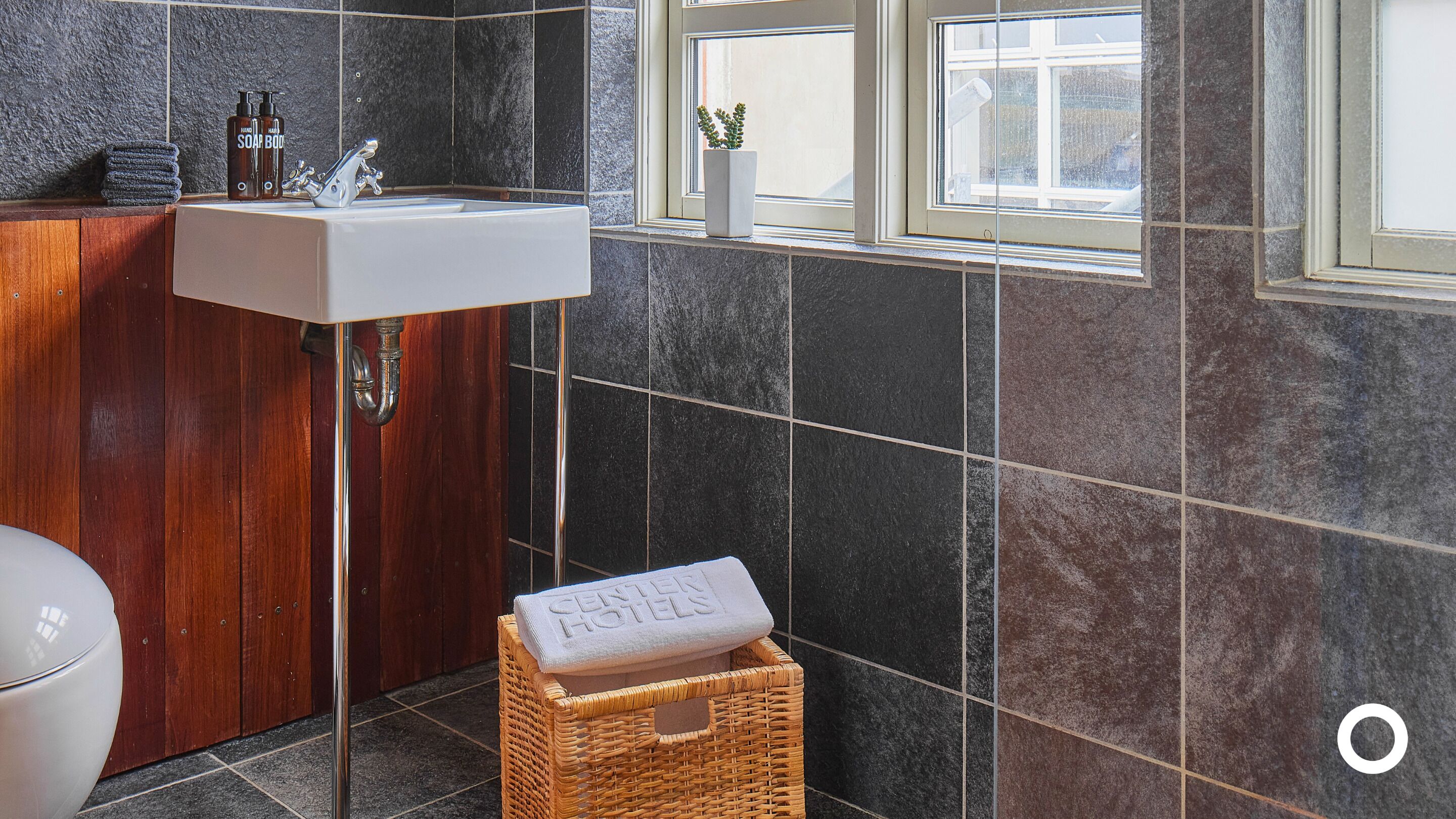 A bathroom with a wooden cabinet, a white sink, and a small wicker basket with a towel.