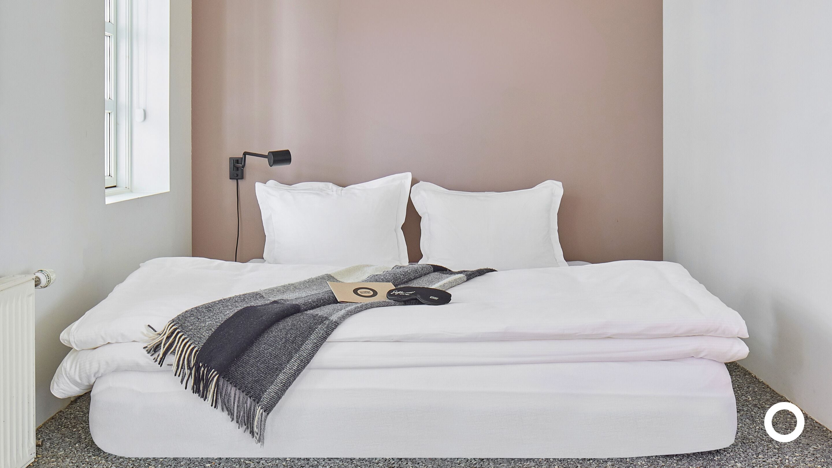 A neatly made bed with white bedding, a grey and black striped blanket, and a black hairbrush.