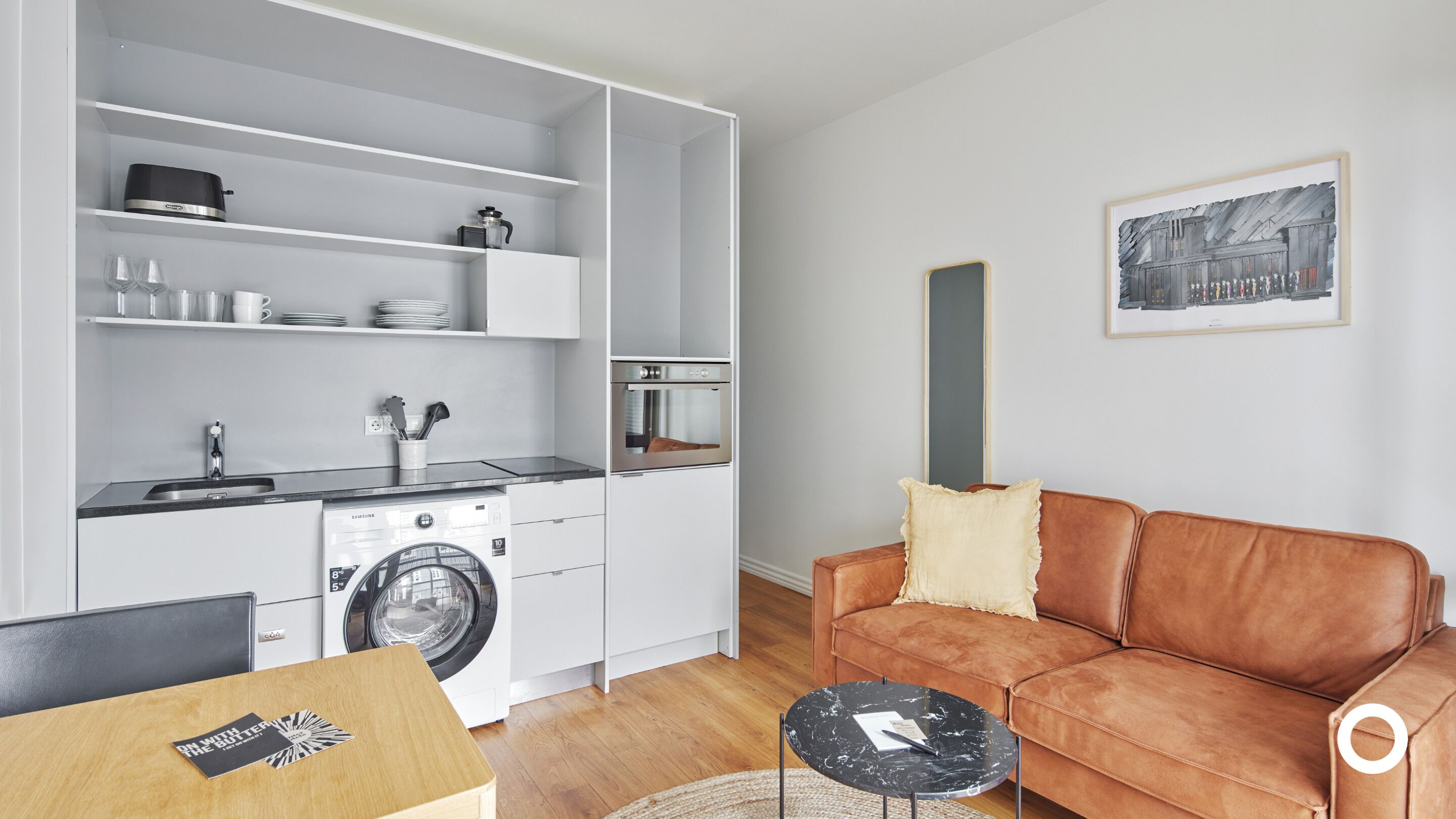 Ein kompakter Wohnbereich mit Küchenzeile, Waschmaschine, Sofa und Couchtisch.
