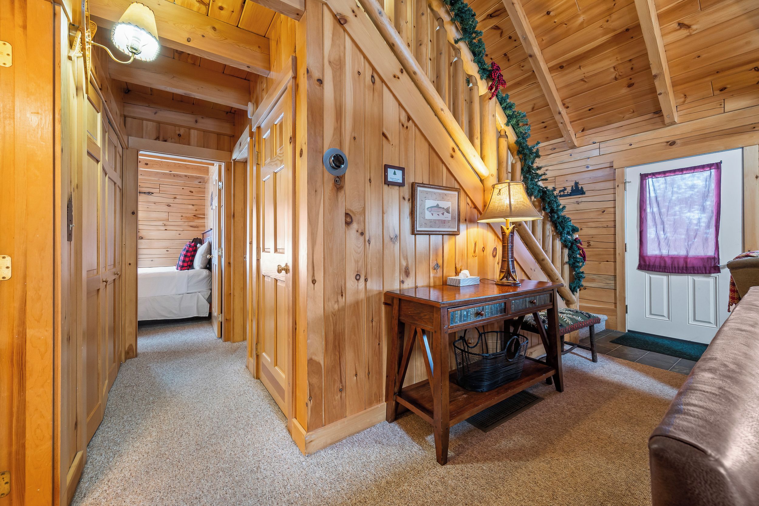 A wooden interior with a staircase, a desk, a bed, and a window with curtains.