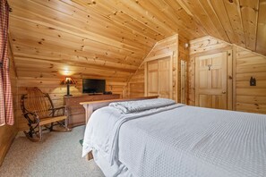 A cozy wooden room with a bed, a desk, a chair, and a television.