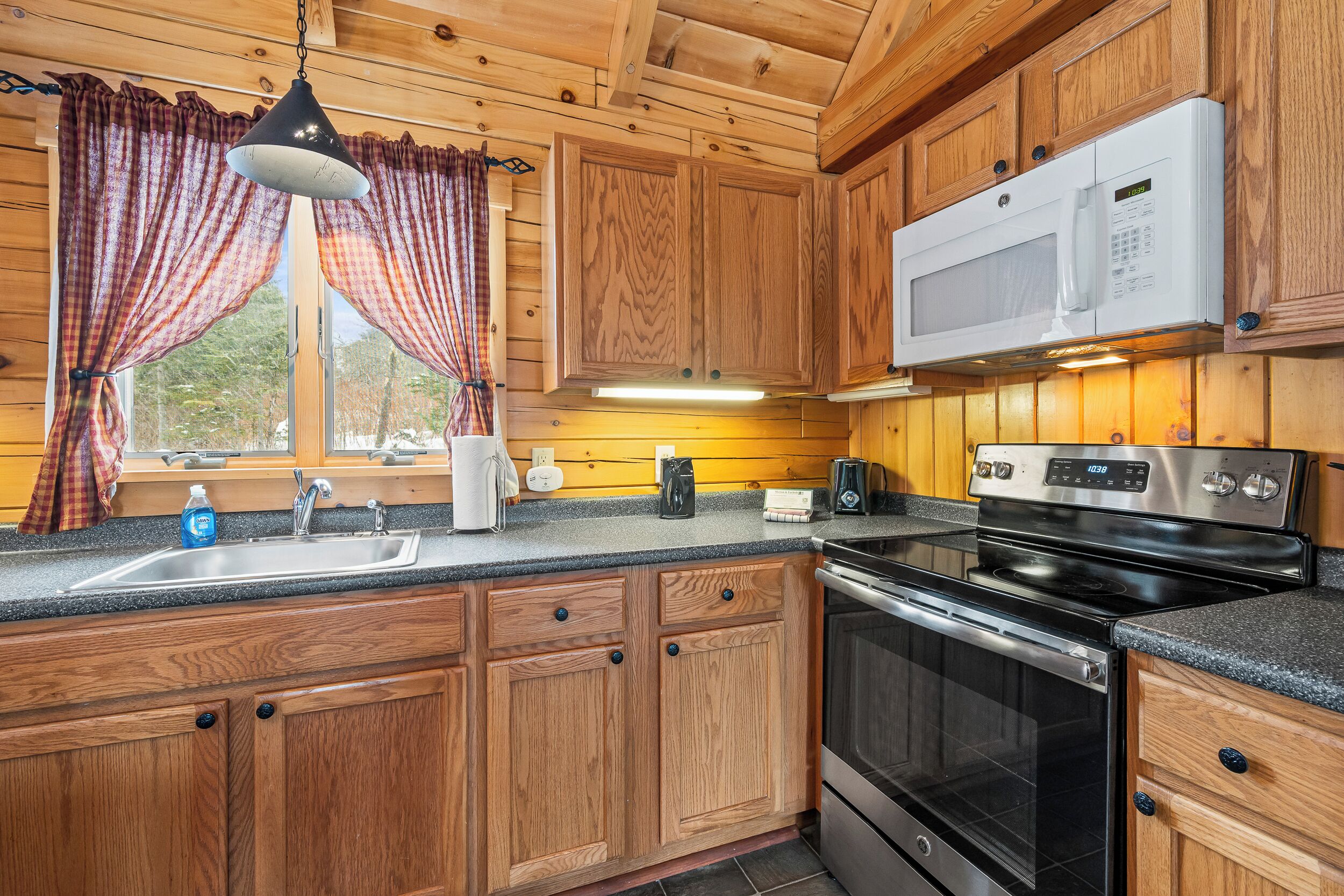 A kitchen with wooden cabinets, a stainless steel sink, a microwave, and a stove.