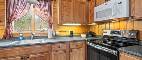 A kitchen with wooden cabinets, a stainless steel sink, a microwave, and a stove.