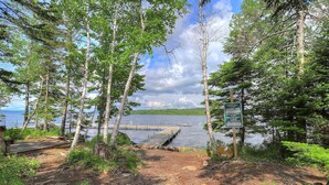 A forested area with a wooden dock extending into a lake, surrounded by birch trees and a sign indicating lakefront rules. - Pine Cabin at Rangeley Lake Resort - shared waterfront on Rangeley Lake (Rangeley)