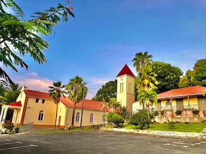 A church with a red roof and a clock tower, surrounded by palm trees and a clear sky.