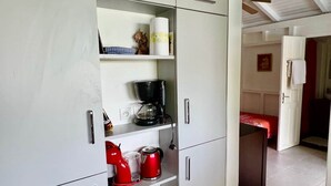 Ett kompakt kök med vita skåp, en kaffebryggare, en brödrost och en röd vattenkokare.
