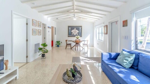 Un vaste espace de vie doté d’un haut plafond, une table à manger avec des chaises, un canapé bleu et un téléviseur posé sur un meuble.