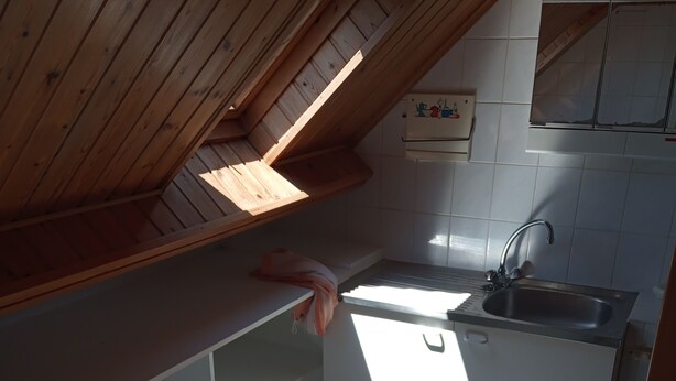 A kitchen with a wooden ceiling, white tiles, a sink, and a towel hanging on the counter. - STUDIO NABIJ STRAND EN CENTRUM (DE PANNE)