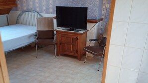 A small, cozy room with a bed, a television, and two chairs. - STUDIO NABIJ STRAND EN CENTRUM (DE PANNE)