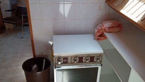 A compact kitchen with a white oven, a trash bin, and a wooden ceiling. - STUDIO NABIJ STRAND EN CENTRUM (DE PANNE)