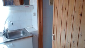 A kitchen with a sink, cabinets, and a wooden door. - STUDIO NABIJ STRAND EN CENTRUM (DE PANNE)