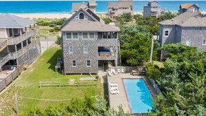A two-story stone building with a pool, surrounded by greenery and a beach view. - Semi-Oceanfront Dog Friendly w/ Saltwater Pool, Hot Tub, Game Room, Volleyball (Avon)