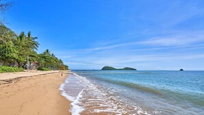 A beach with clear blue water, palm trees, and a distant island. - 2 Bedroom Oceanfront Penthouse Beach Club (Palm Cove)