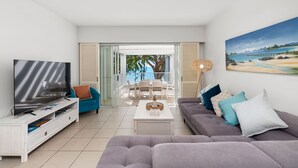 A modern living room with a TV, sofa, and a balcony with a view of the sea. - 2 Bedroom Oceanfront Penthouse Beach Club (Palm Cove)