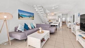A modern living room with a sofa, coffee table, and a staircase leading to a kitchen. - 2 Bedroom Oceanfront Penthouse Beach Club (Palm Cove)