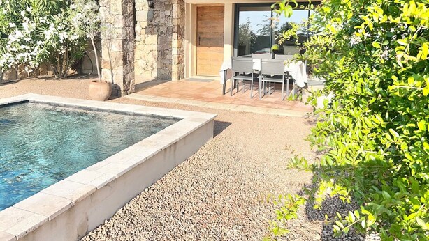 Una piscina con borde de piedra, un muro de piedra y un patio con mesa y sillas.