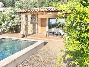 A pool with a stone border, a stone wall, and a patio area with a table and chairs. - Mini-villa with a pool right on the water (Sari-Solenzara)