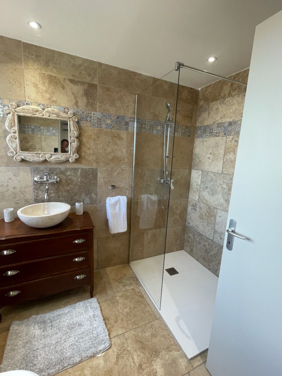 A modern bathroom with a glass shower enclosure, a marble sink, and a vanity with drawers.