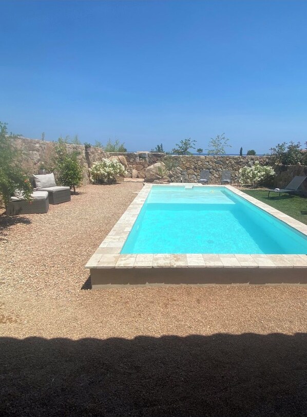 A rectangular swimming pool with a stone border, surrounded by a gravel area and a stone wall. - Mini-villa with a pool right on the water (Sari-Solenzara)
